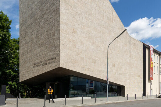 A stone-clad museum building with a glass entrance at street level